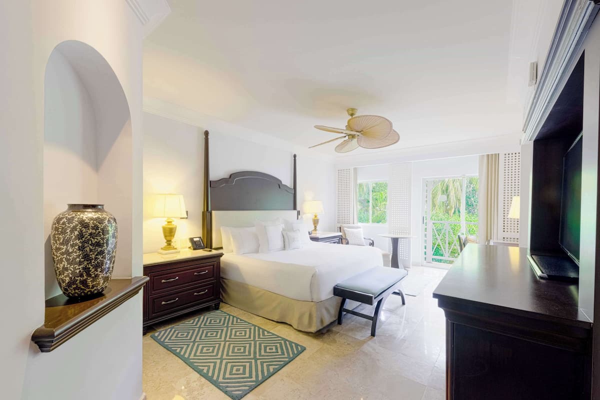 Une chambre d’hôtel équipée d’un lit, de tables de chevet, d’une télévision, d’un ventilateur de plafond et offrant une vue sur la verdure environnante.