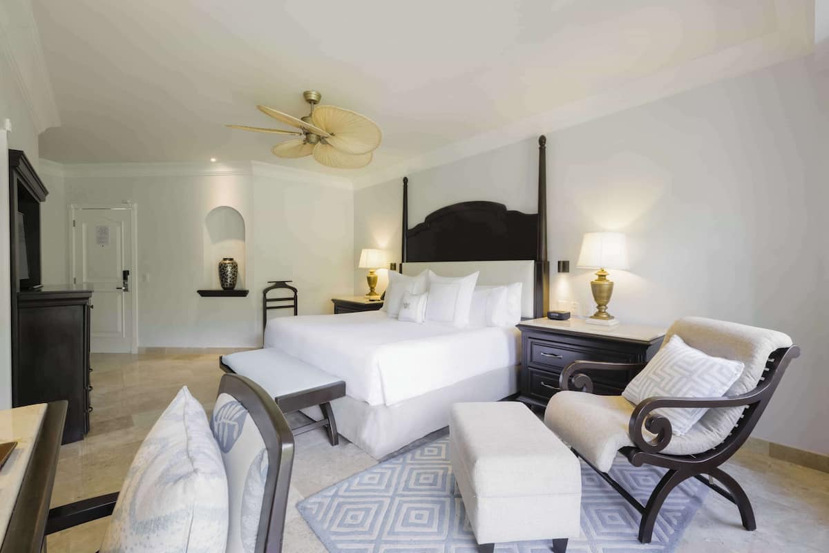Une chambre d’hôtel comprenant un lit, des tables de chevet, un bureau, une chaise et un ventilateur de plafond.