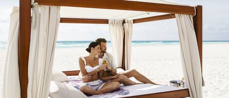 A wooden bed with a canopy, white bedding, and a view of the beach and ocean.
