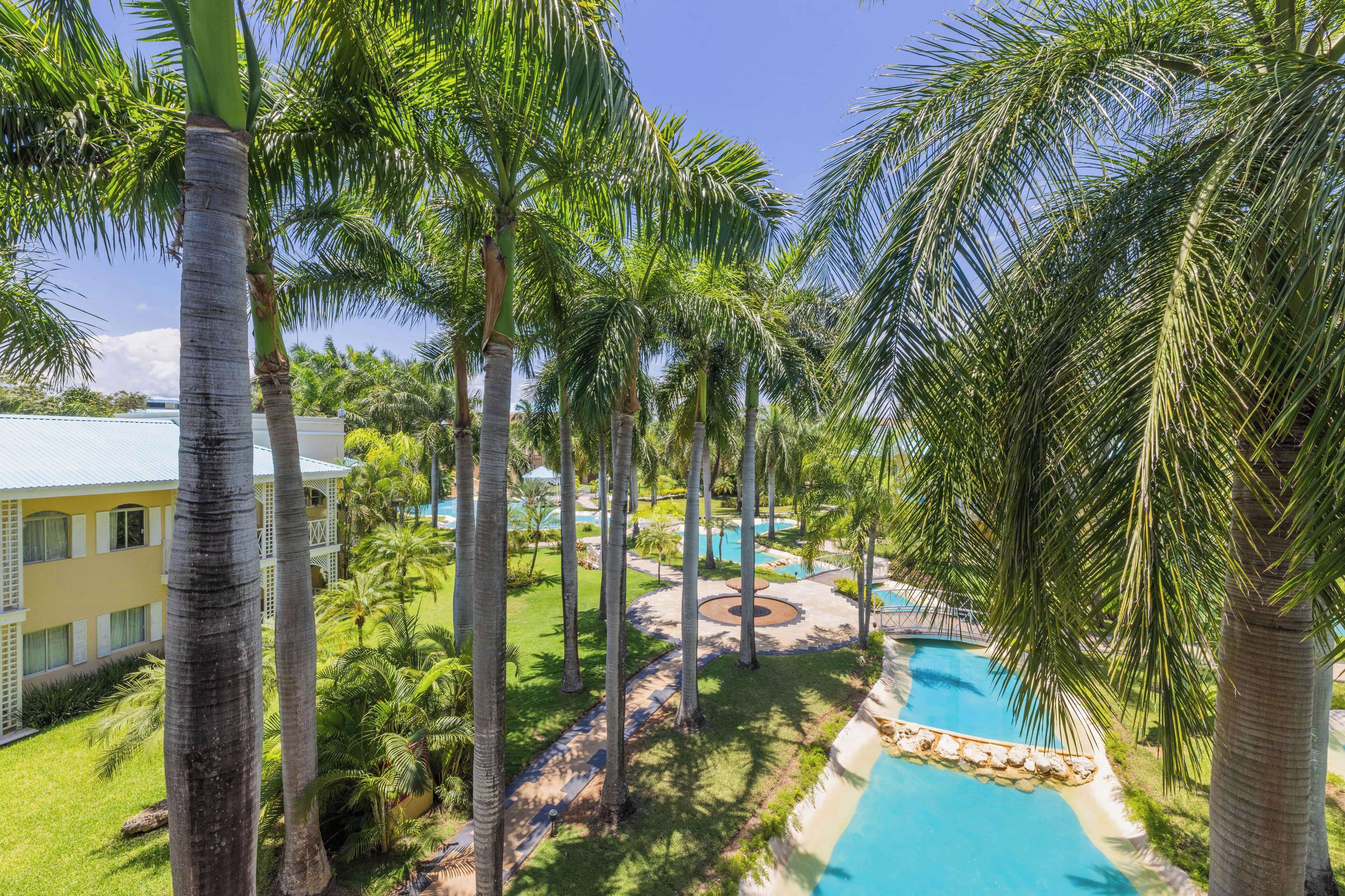 Un resort con piscina rodeada de palmeras y un edificio de fachada amarilla.