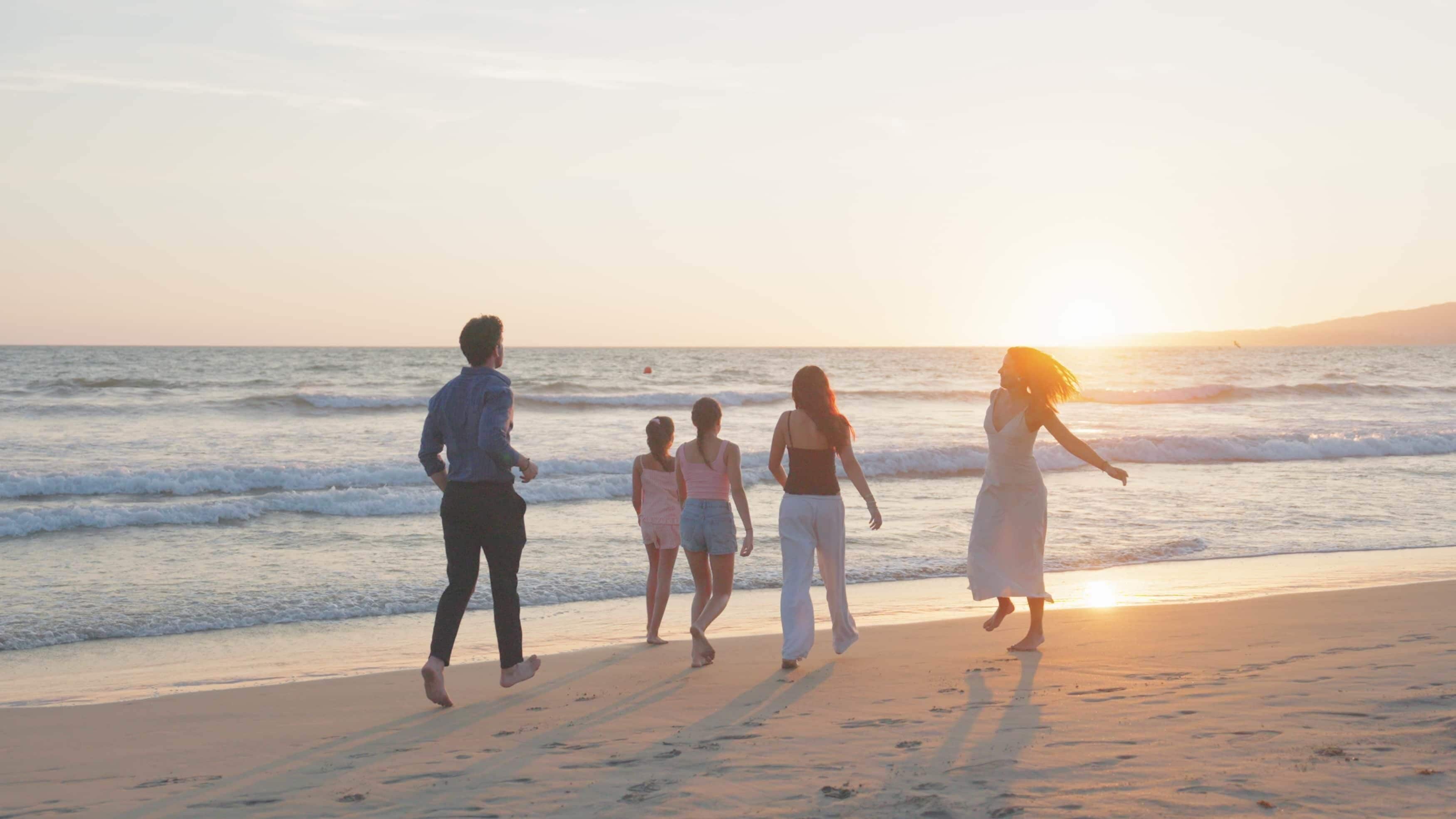 A family walking on a beach at sunset.