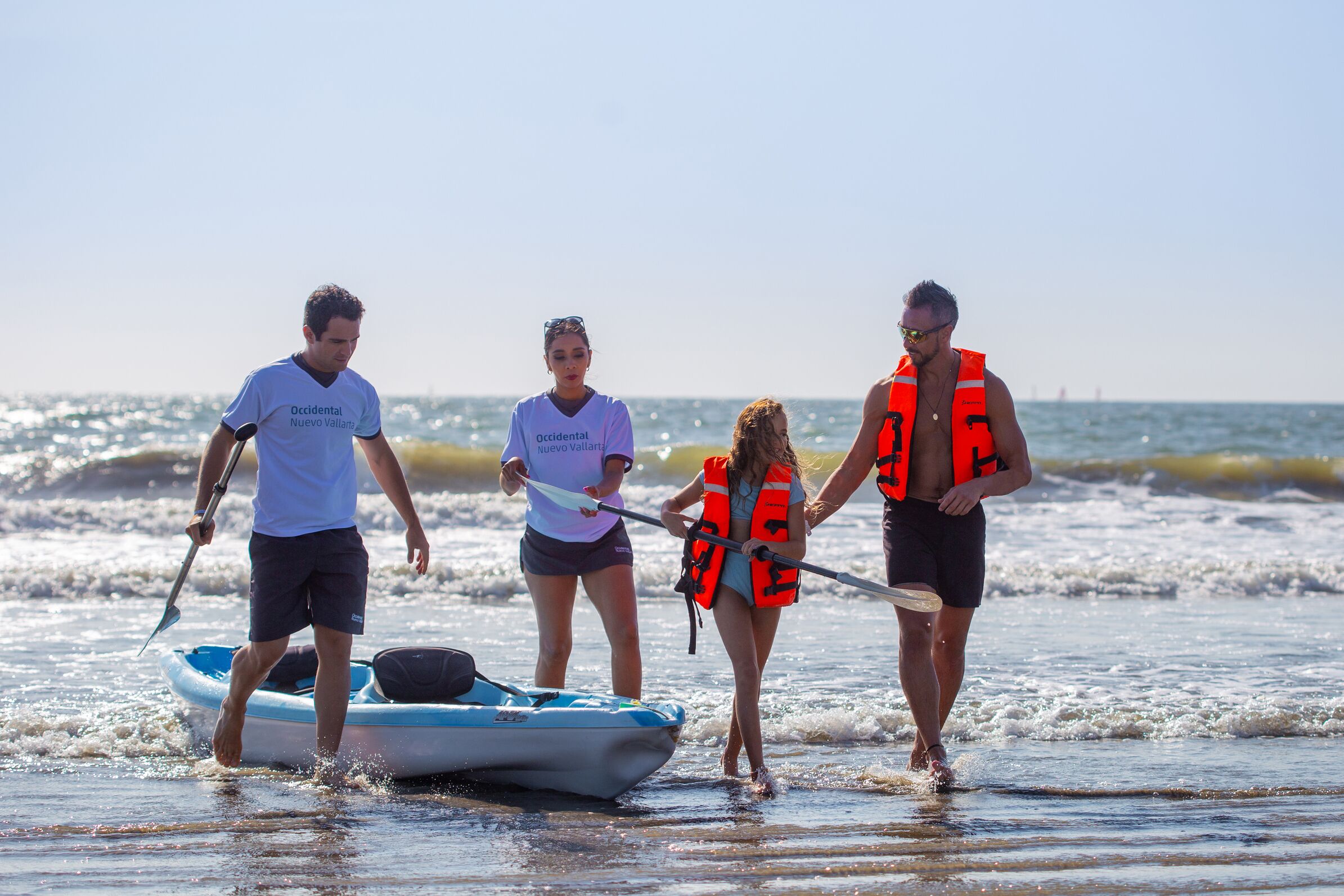 A group of people on a beach with a boat and paddleboards.