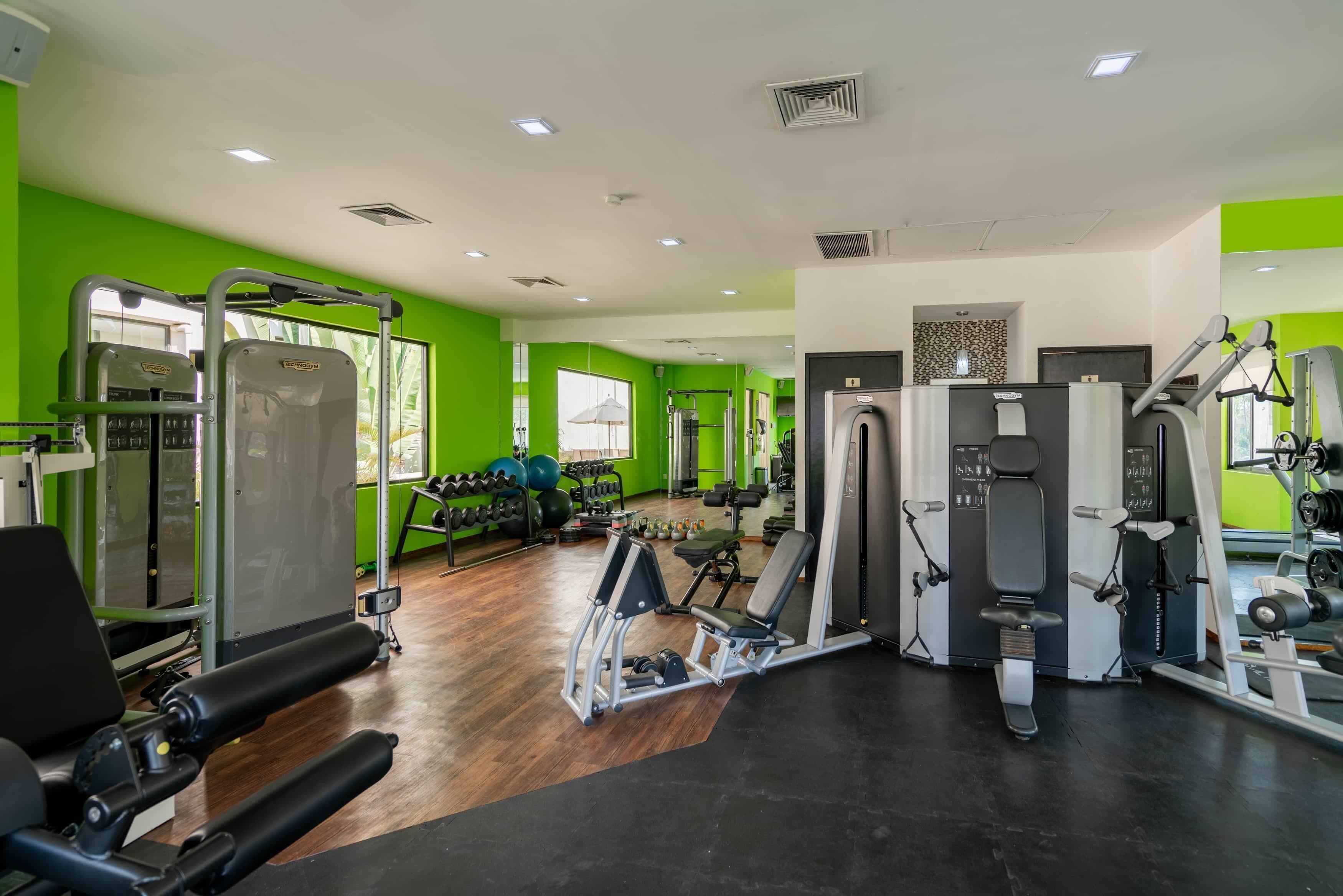 Une salle de sport équipée de divers appareils d’exercice, de supports à poids et dotée d’un mur entièrement recouvert de miroirs.