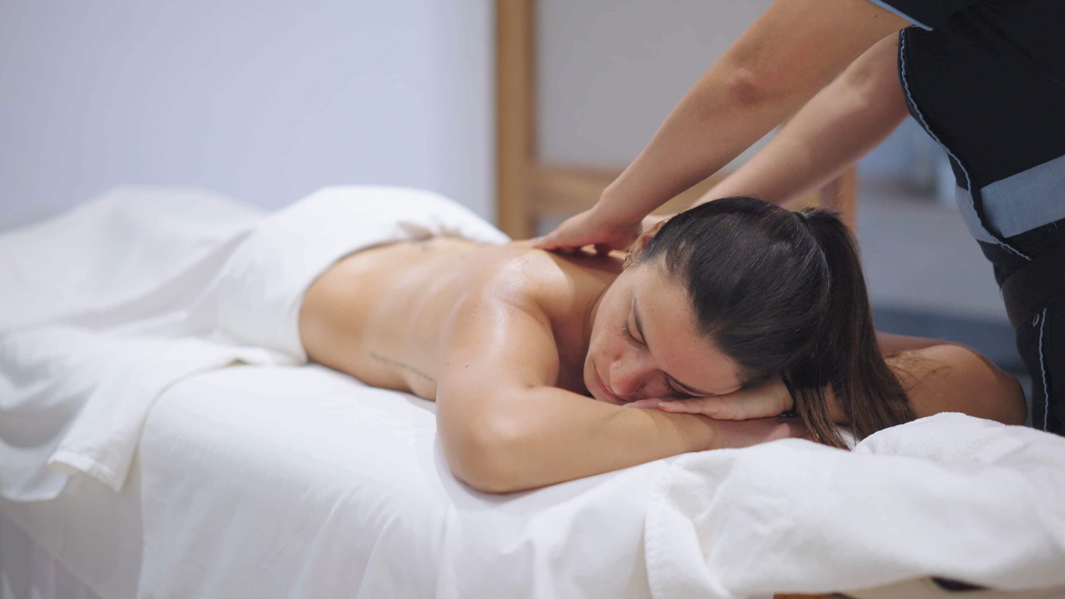 A person receiving a back massage on a bed in a room with white bedding.