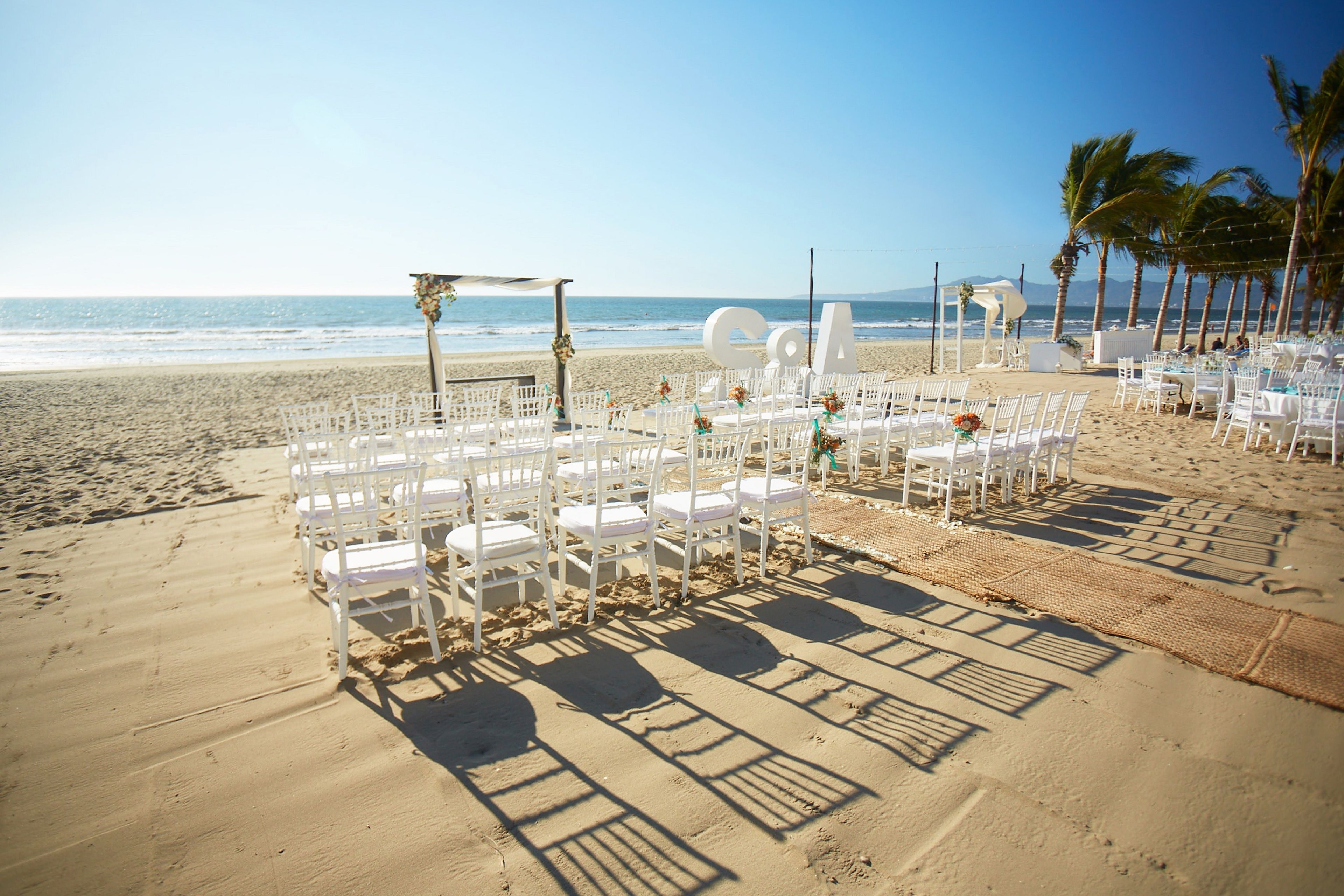 A beach wedding setup with white chairs and a canopy.