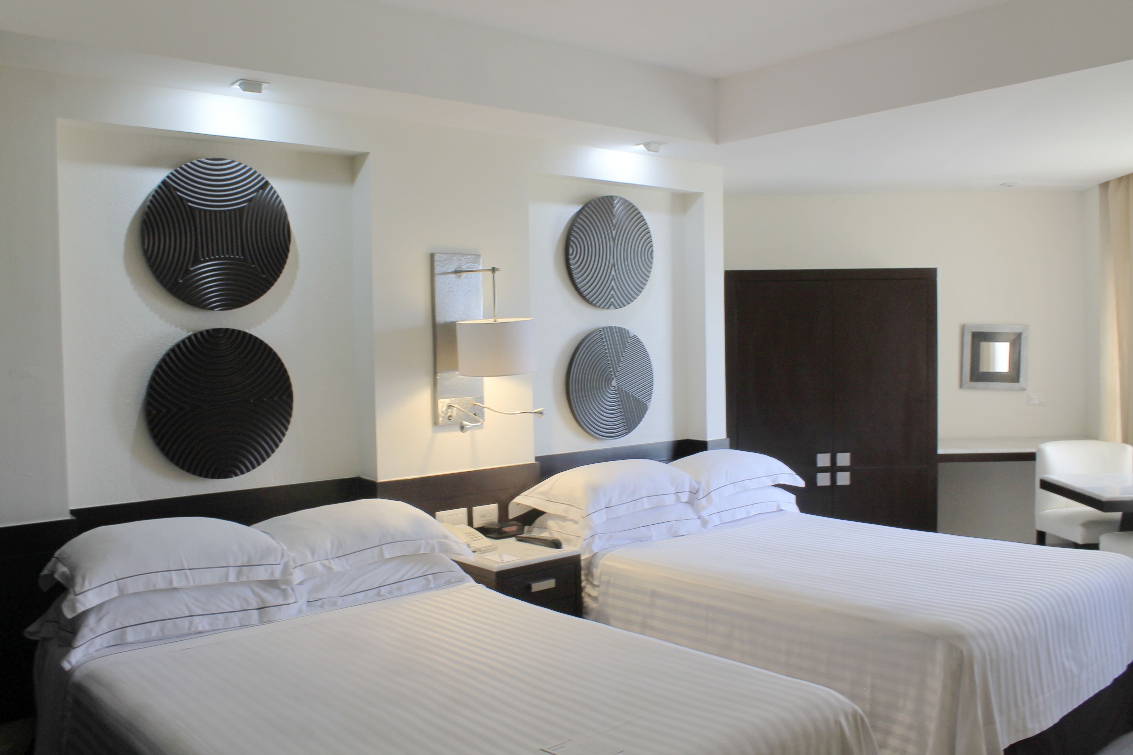 Een hotelkamer met twee bedden, een bureau en een stoel. Er hangen decoratieve borden aan de muur en er is een spiegel.