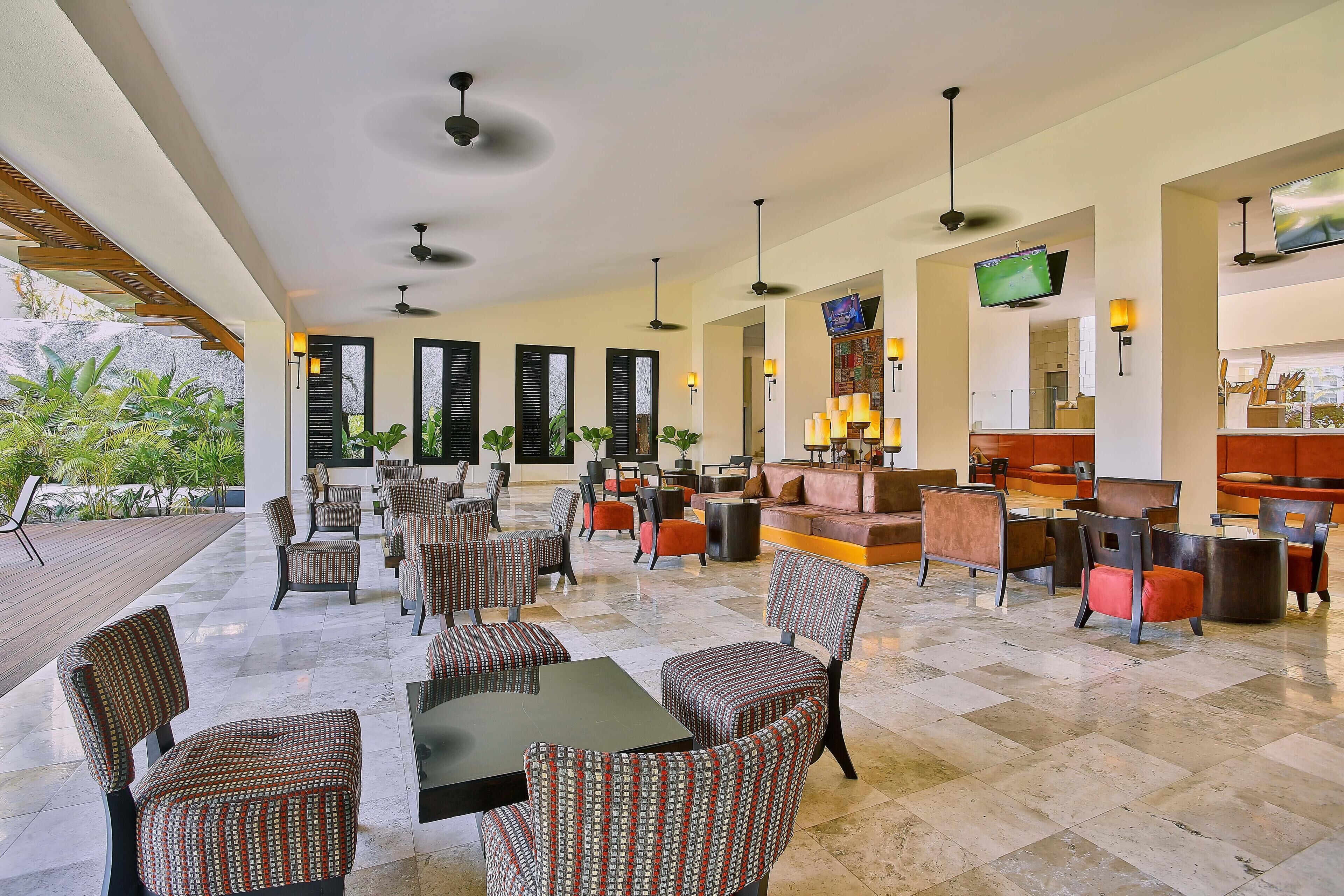 A spacious indoor area with multiple seating arrangements, including tables and chairs, and a television mounted on the wall.