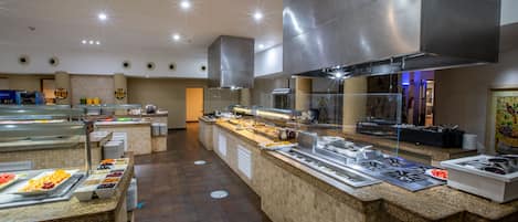 A buffet area with various food stations, a large stainless steel range hood, and a tiled floor.