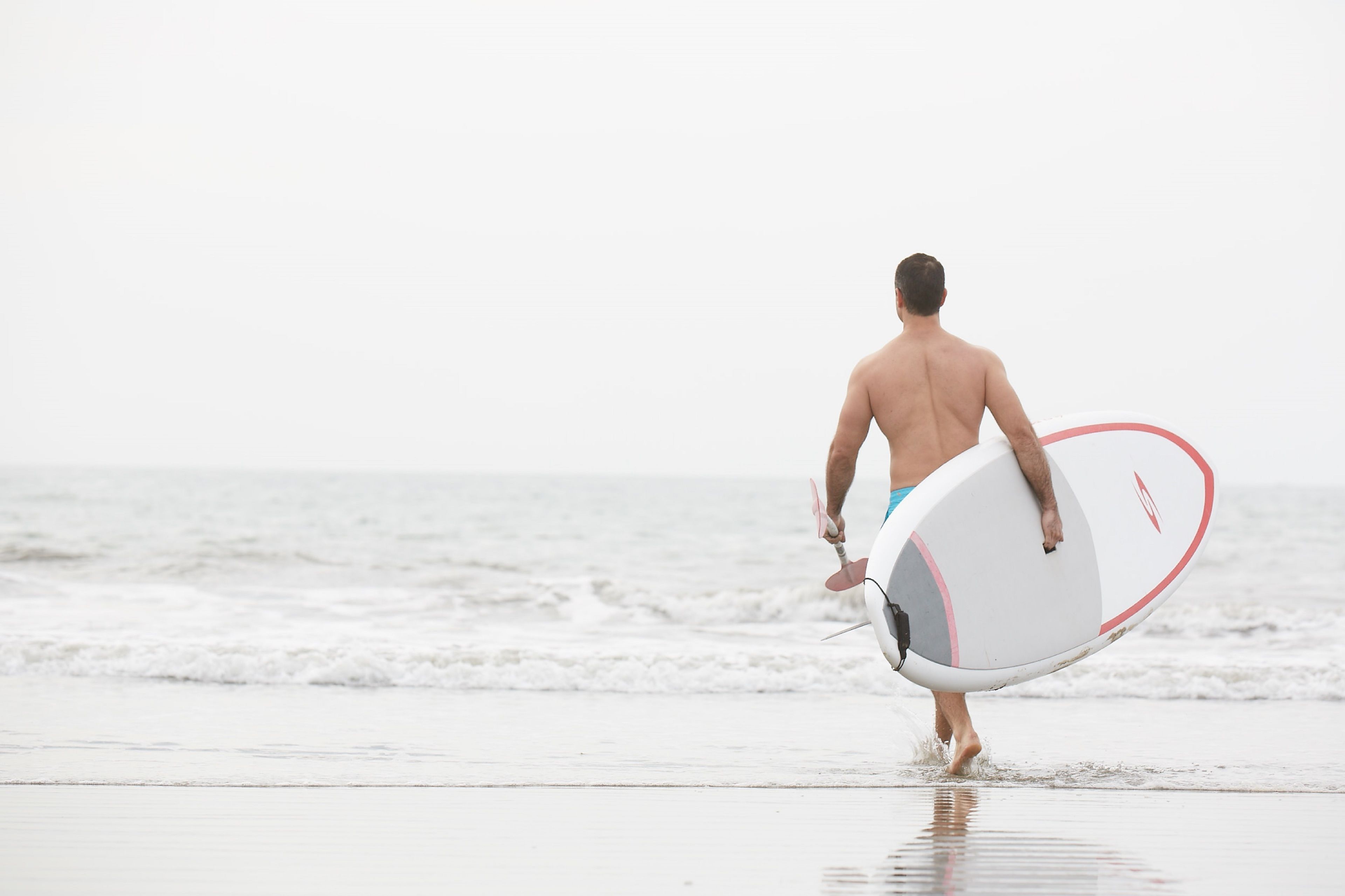 Un hombre caminando por la playa llevando una tabla de surf.