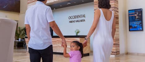 Une famille se tient la main devant un comptoir d’accueil sur lequel est affiché un panneau indiquant « OCCIDENTAL NUEVO VALLARTA ».