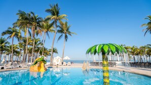 A pool with palm trees, lounge chairs, and a slide. - Occidental Nuevo Vallarta - All Inclusive (Nuevo Nayarit)