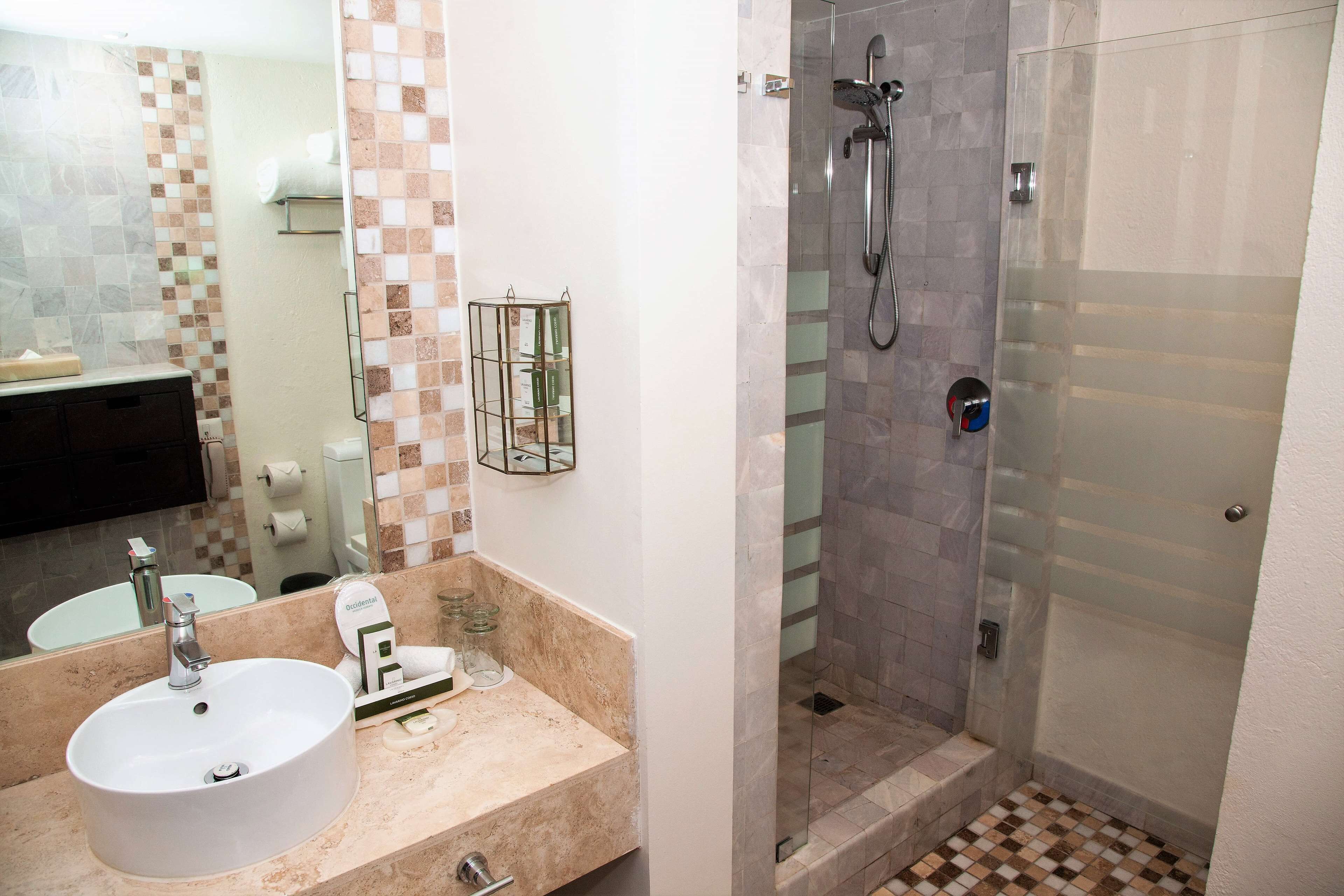 A bathroom with a sink, mirror, glass shower enclosure, and tiled walls.