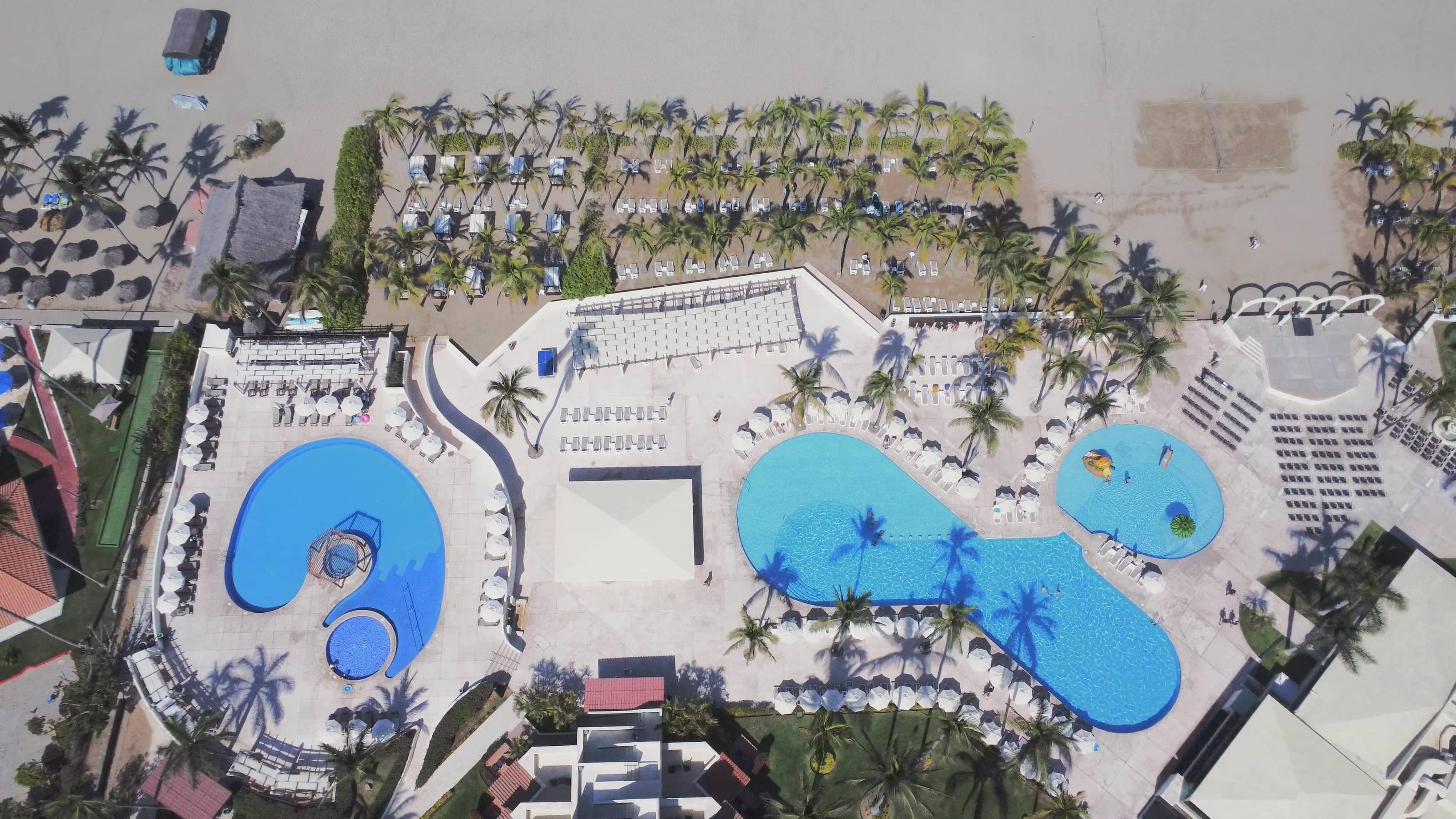 A resort with multiple swimming pools, sun loungers, and palm trees.