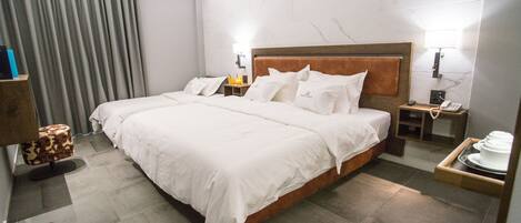 A hotel room with a large bed, two bedside tables, a nightstand, a lamp, and a tray with dishes.