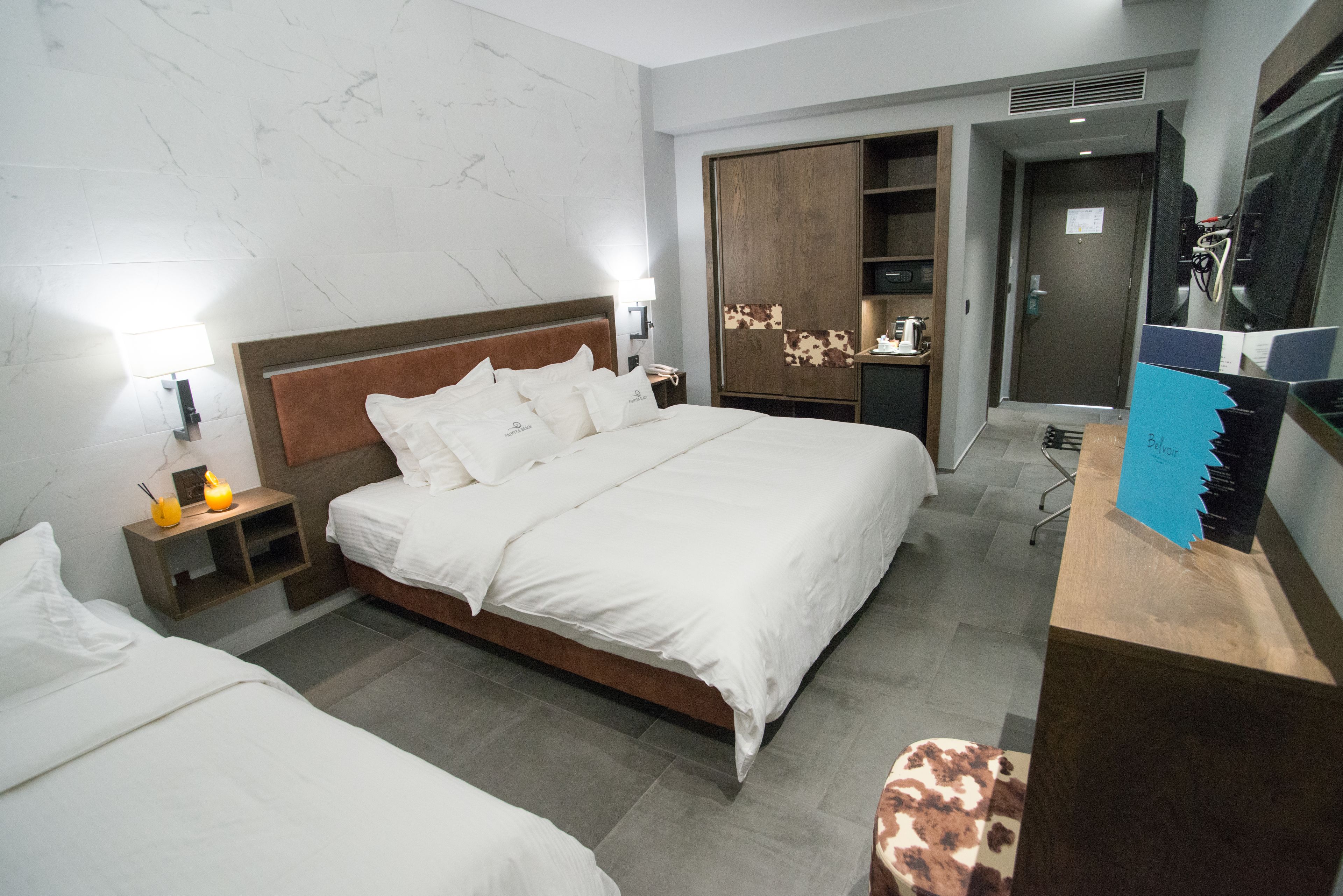 A hotel room with a large bed, a wooden wardrobe, a desk with a computer, and a small seating area.