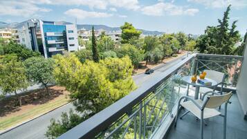 A balcony with a glass railing overlooking a road with cars, trees, and buildings.