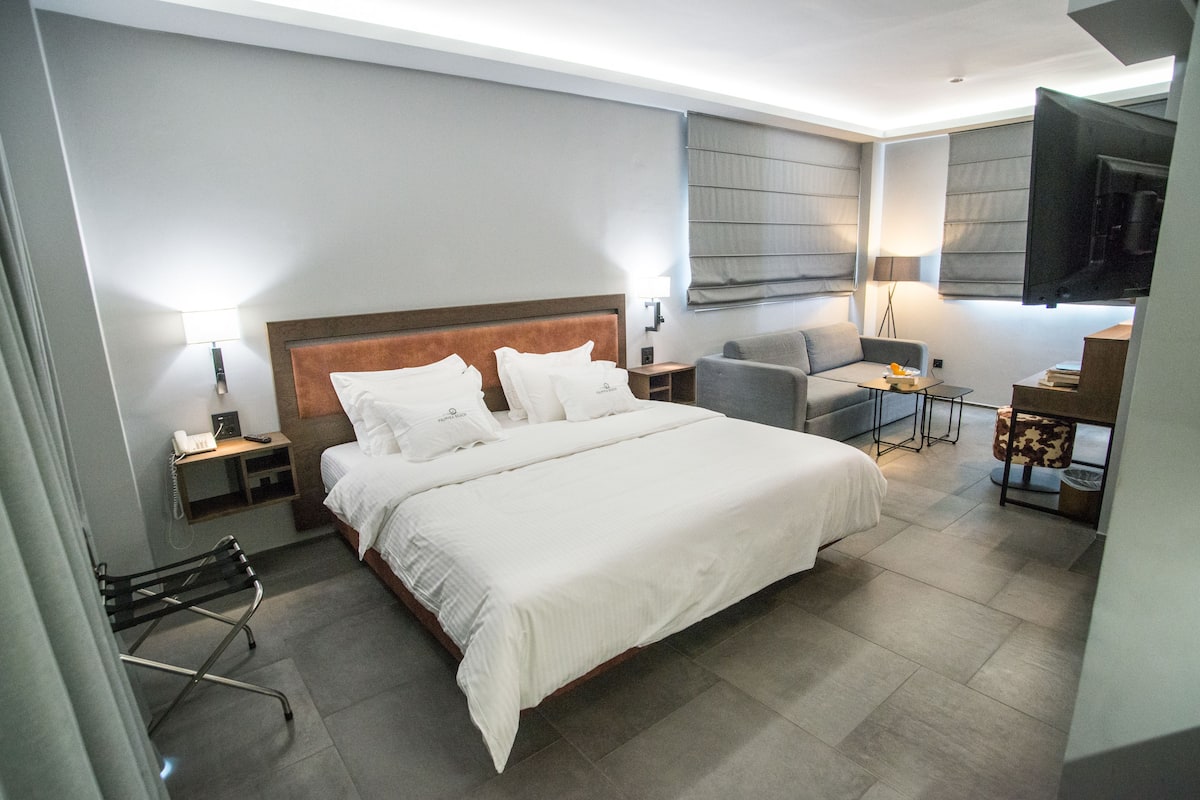 A modern hotel room with a large bed, a desk, a chair, and a TV.
