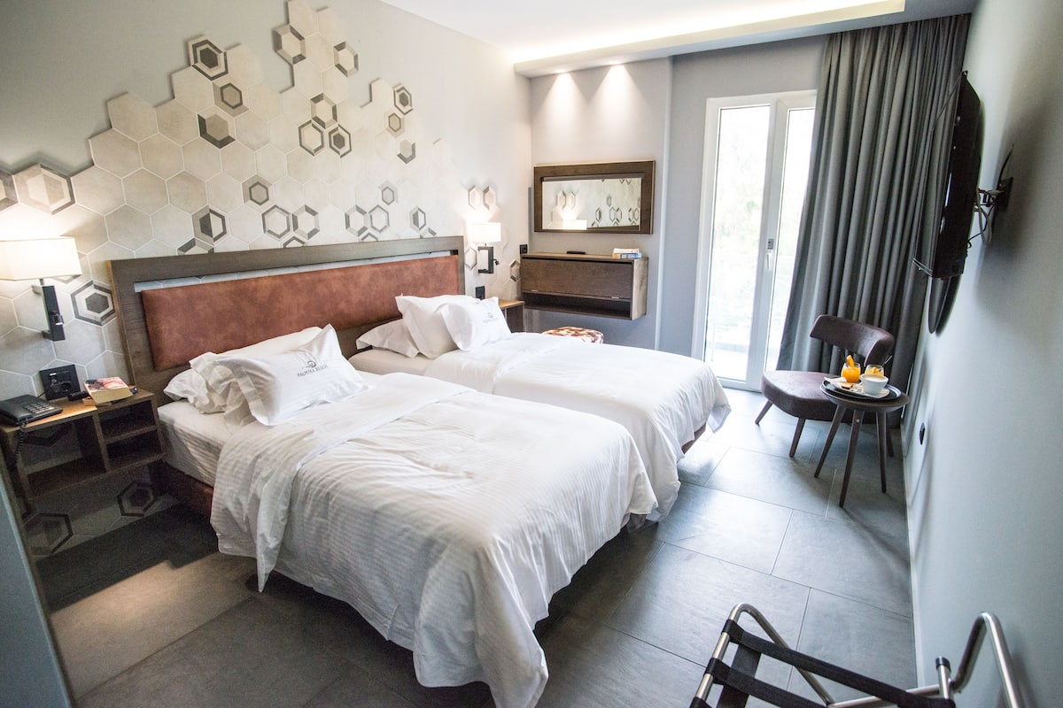 A hotel room with two beds, a desk, a chair, a TV, and a bathroom with a shower and toilet.