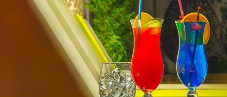 Two colorful cocktails with straws and lemon slices, ice cubes, and a glass of water.