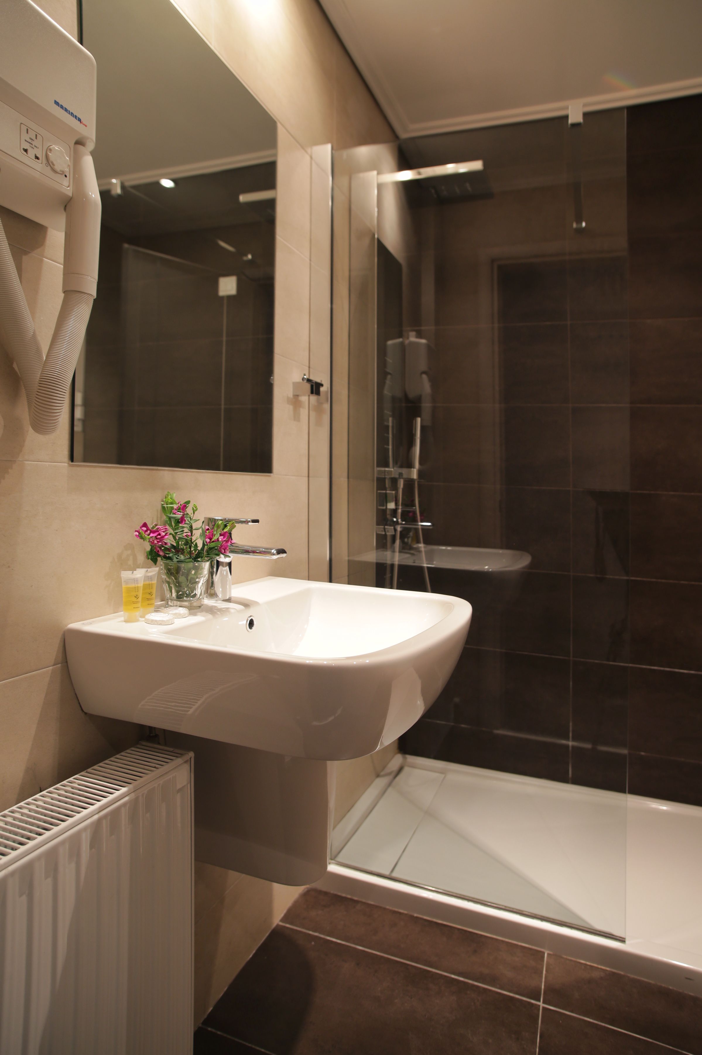 Un baño moderno con un lavabo blanco, una cabina de ducha con mampara de vidrio y un radiador.