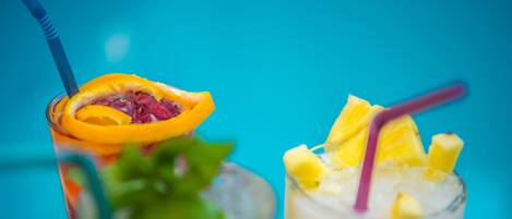 Two glasses of iced beverages with fruit slices and straws.