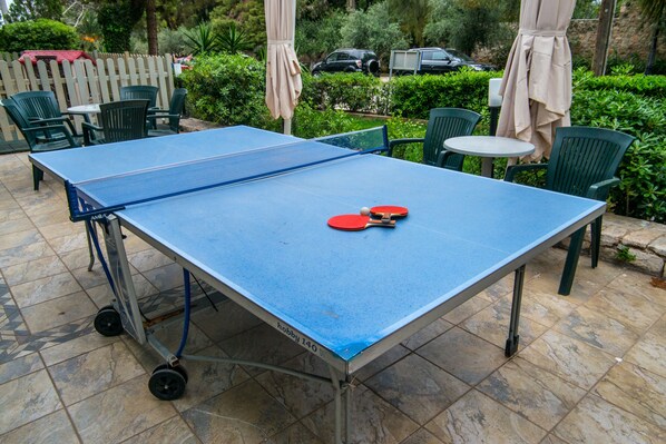 A ping pong table with two red paddles and a ball, surrounded by green chairs and a small table. - Hotel Palmyra Beach (Glyfada)
