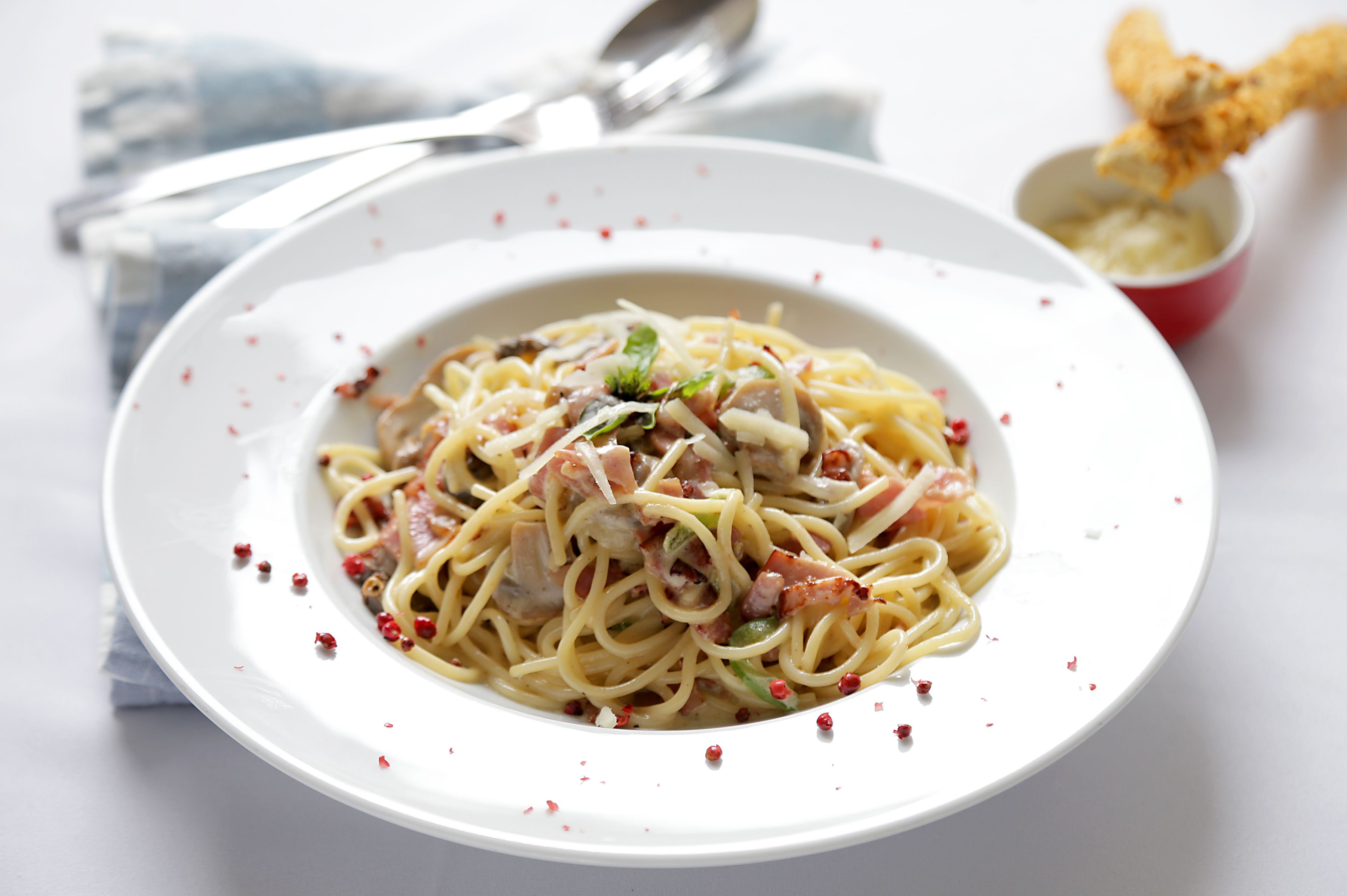 Une assiette de spaghettis avec de la viande et des légumes, une fourchette et un petit bol de sauce.