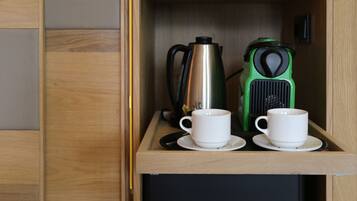 Un mueble de madera con dos tazas blancas en platillos y dos cafeteras, una verde y una plateada.