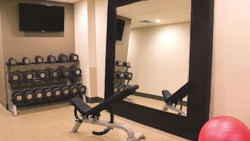 A gym with a bench, dumbbells, a red exercise ball, and a large mirror.