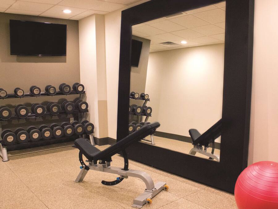 A gym with a bench, dumbbells, a red exercise ball, and a large mirror.