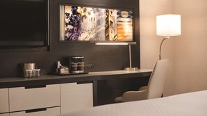 A hotel room with a modern desk, a flat-screen TV, a coffee maker, and a lamp.