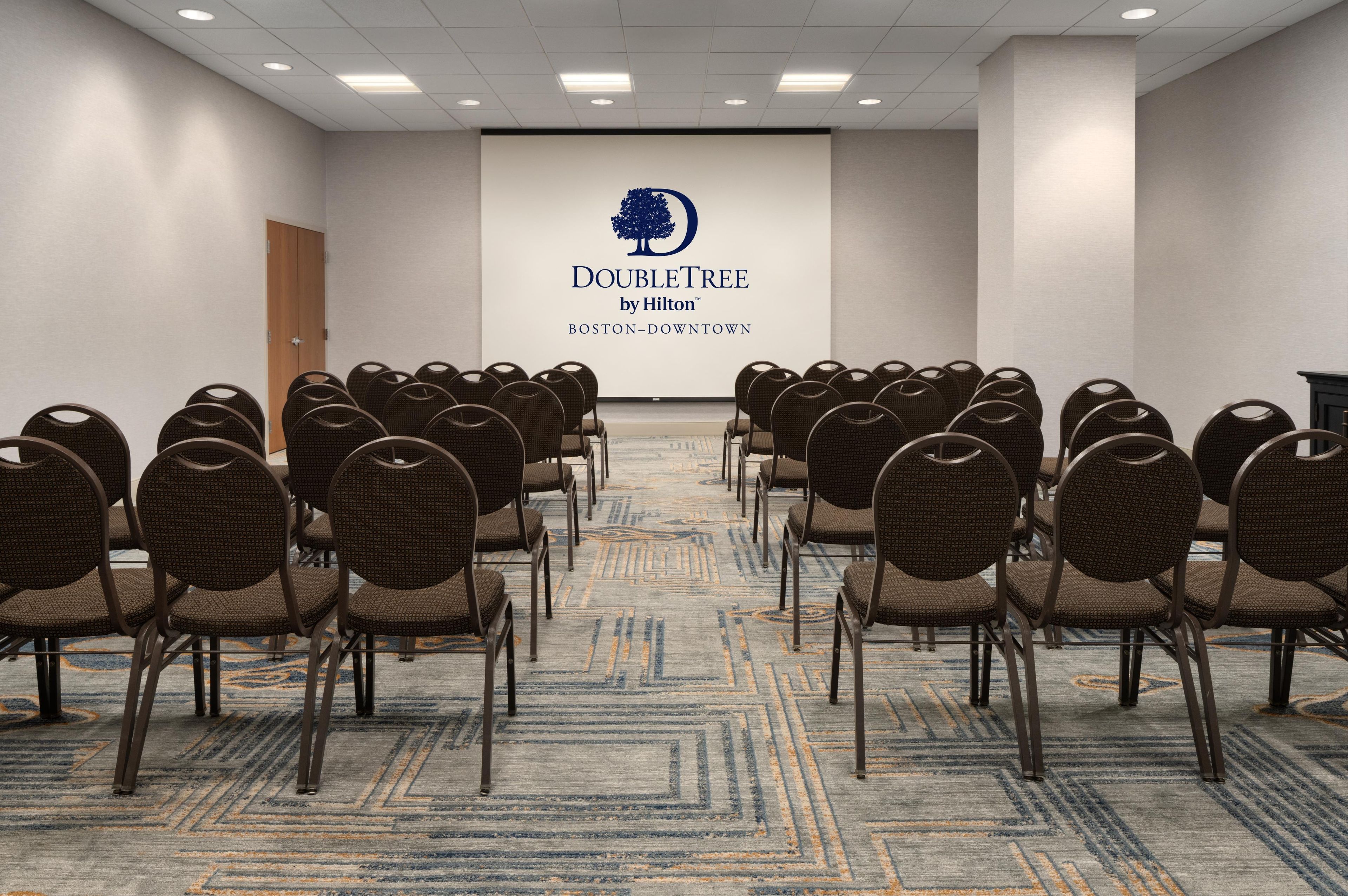 Un salón de conferencias con filas de sillas apuntando a una pantalla que muestra el logotipo de DoubleTree by Hilton.