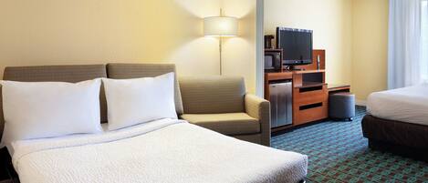 Habitación de hotel con una cama grande, un sofá, un escritorio con televisor y una lámpara.