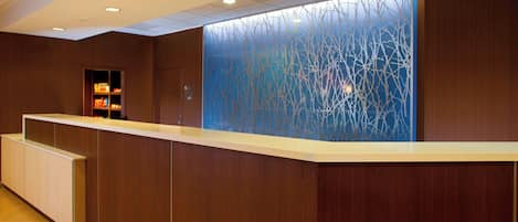 A reception area with a wooden reception desk, a glass partition with a tree branch design, and a shelf with items.