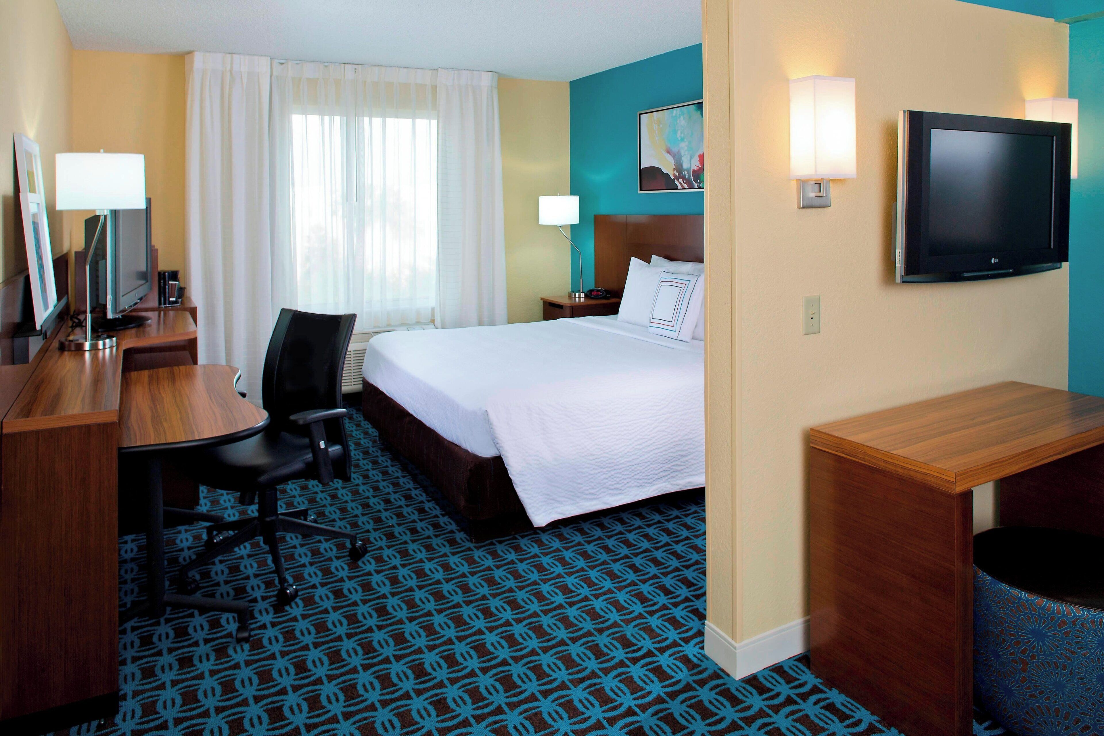A hotel room with a bed, desk, chair, TV, and lamps.