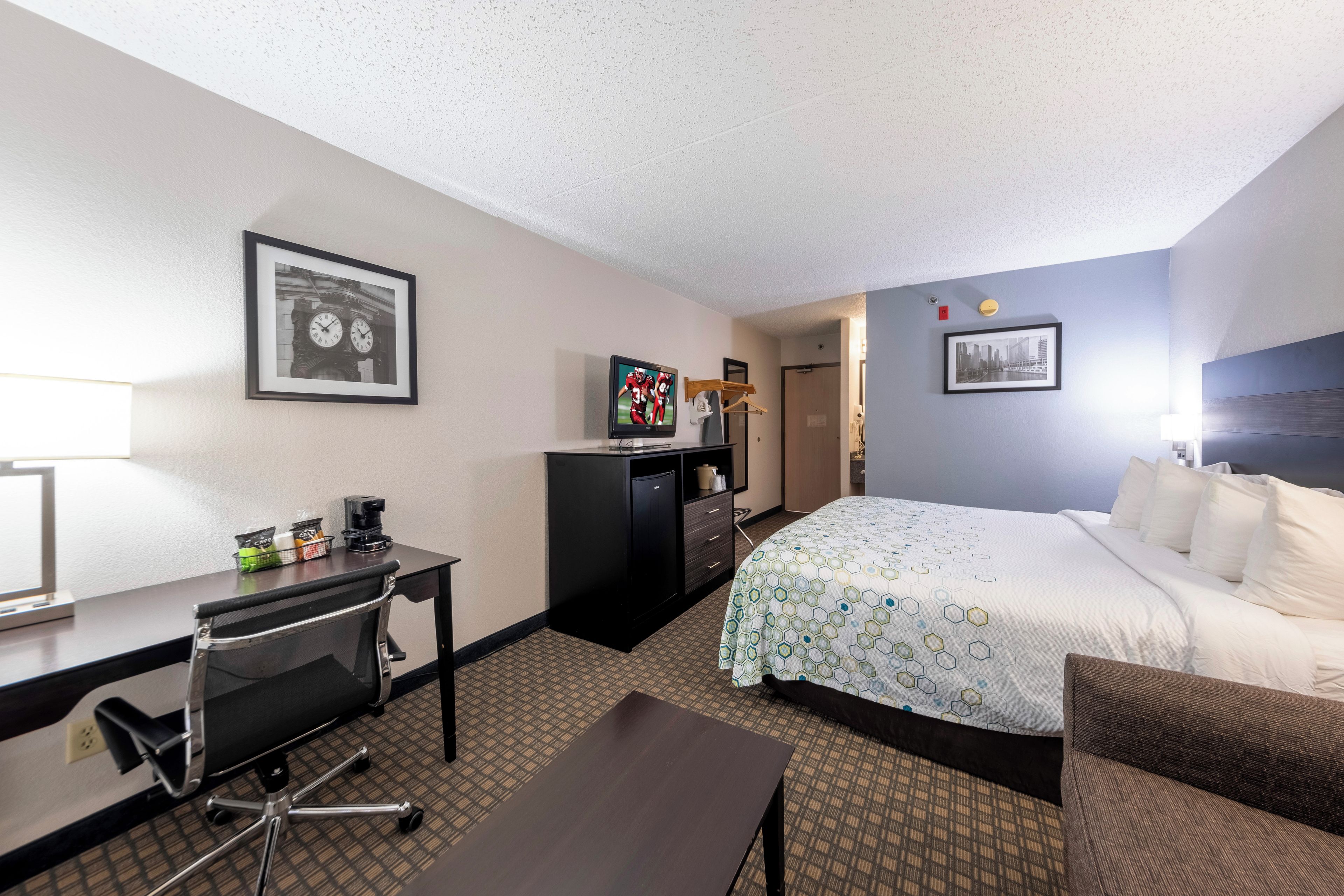A hotel room with a bed, desk, chair, and a television.