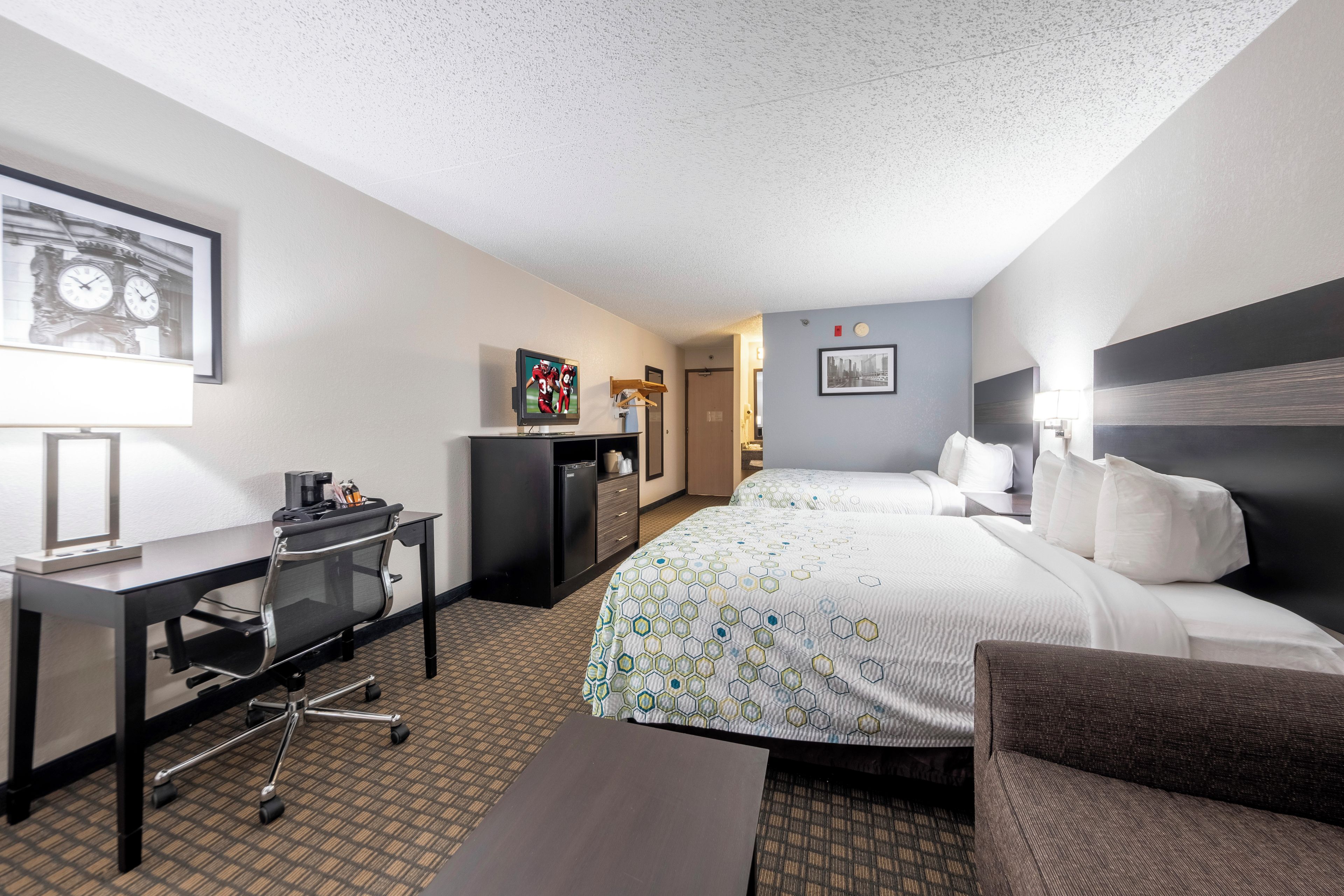 A hotel room with a bed, desk, chair, and a small kitchenette.