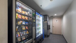 Een gang met automaten voor snacks en drankjes, een deur en een betegelde vloer.
