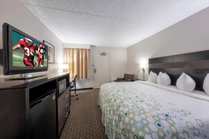 Una habitación de hotel con una televisión sobre un escritorio, una cama con colcha estampada, un escritorio con una silla y una puerta.