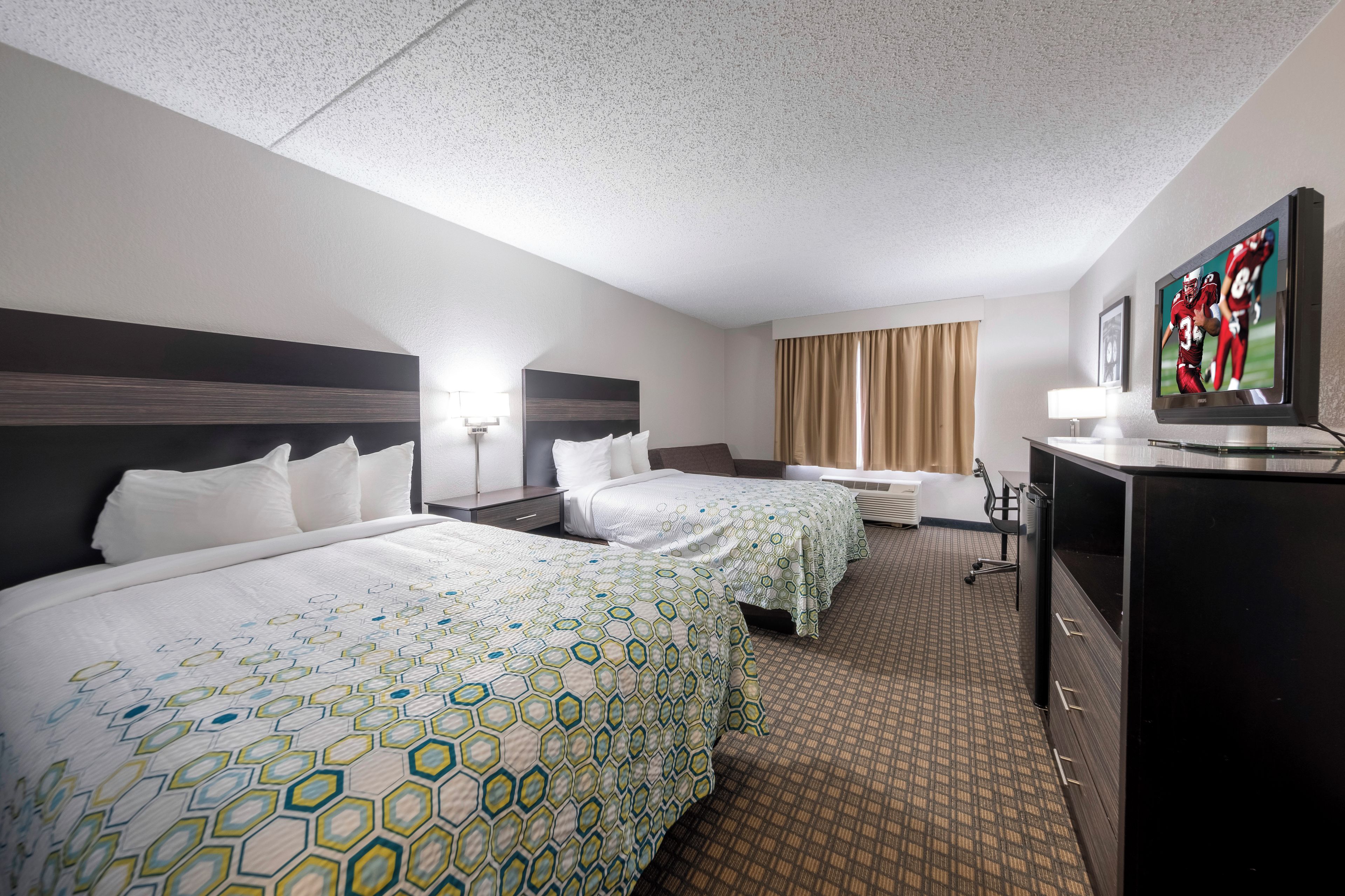 A hotel room with two beds, a desk, a television, and a window with curtains.