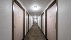 Een hotelgang met tapijtvloeren, houten deuren en een plafondlamp.