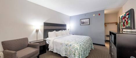 A hotel room with a bed, a chair, a desk, a lamp, a television, and a picture on the wall.