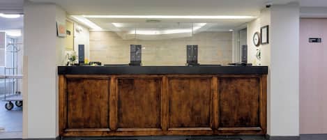A reception desk with a wooden finish, a glass partition, and a clock on the wall.