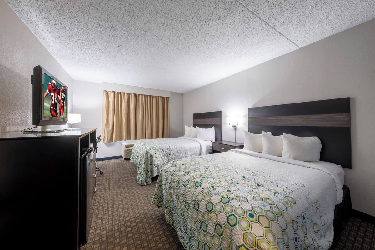 Habitación de hotel con dos camas, televisión, escritorio y ventana con cortinas.