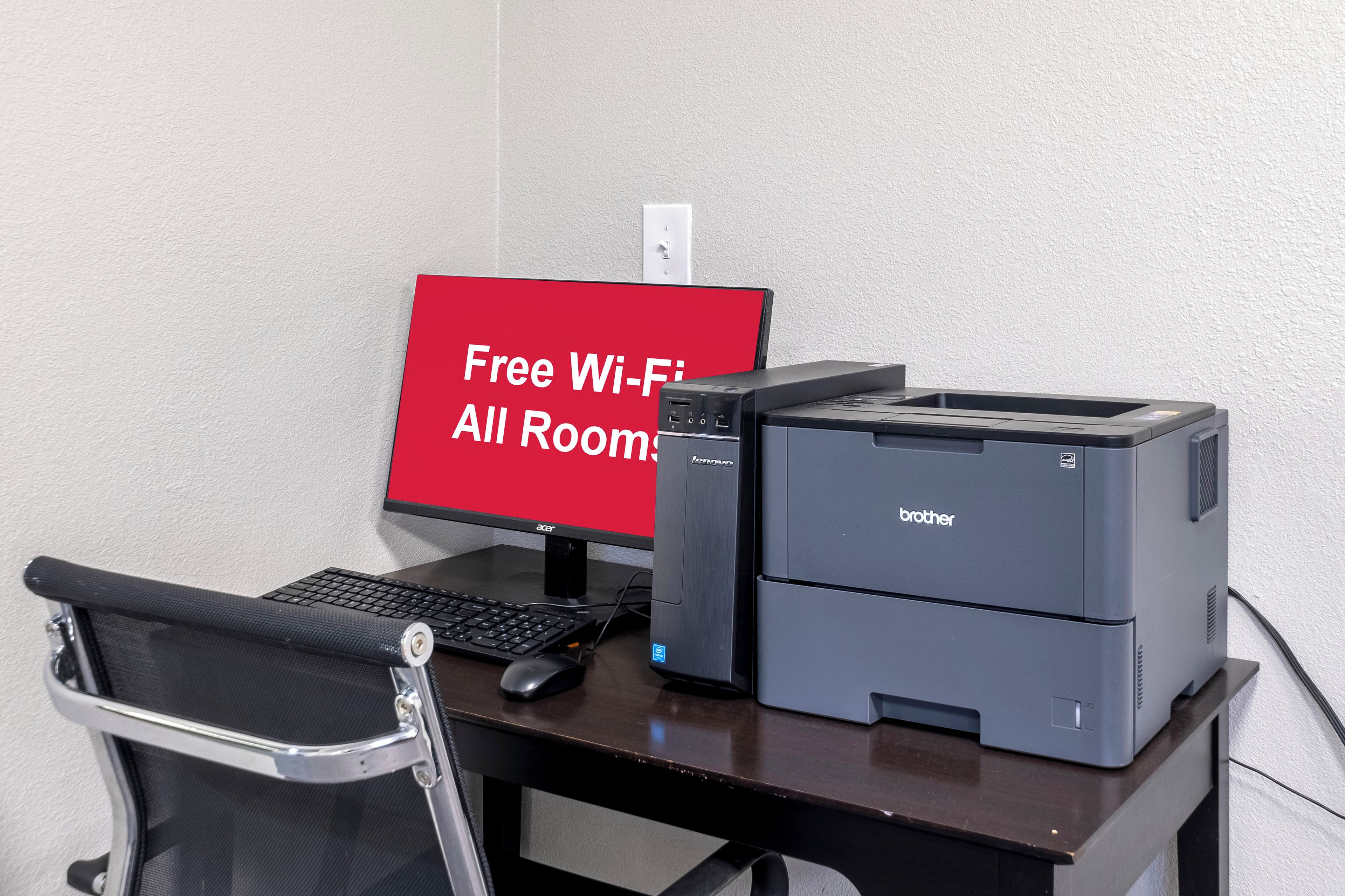 Un escritorio con una computadora, una impresora y un letrero que indica Wi-Fi gratuito en todas las habitaciones.