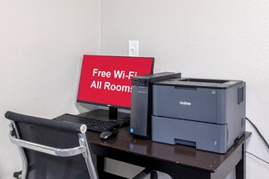 Un escritorio con una computadora, una impresora y un letrero que indica Wi-Fi gratuito en todas las habitaciones.