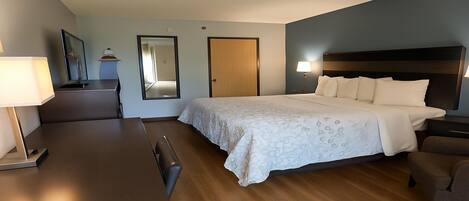 A hotel room with a bed, a desk, a chair, a dresser, and a mirror.