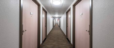 Un pasillo de hotel con pisos alfombrados, puertas de madera y un plafón con lámpara.