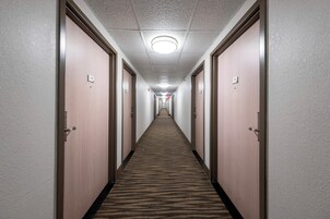 A hotel hallway with carpeted floors, wooden doors, and a ceiling with a light fixture.