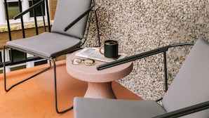 A balcony with two grey chairs, a small round table with a newspaper, a black mug, and a pair of glasses.
